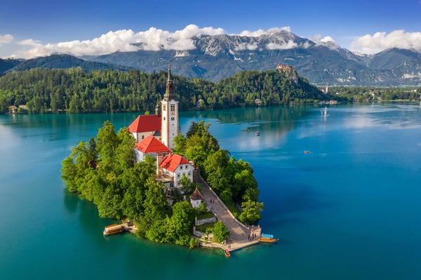 Kleine Insel mit Kirche im türkisblauen Bleder See, umgeben von grünen Wäldern und Bergen
