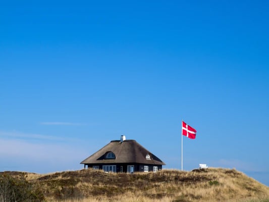 Reetgedecktes Haus in den Dünen mit dänischer Flagge vor klarem blauem Himmel