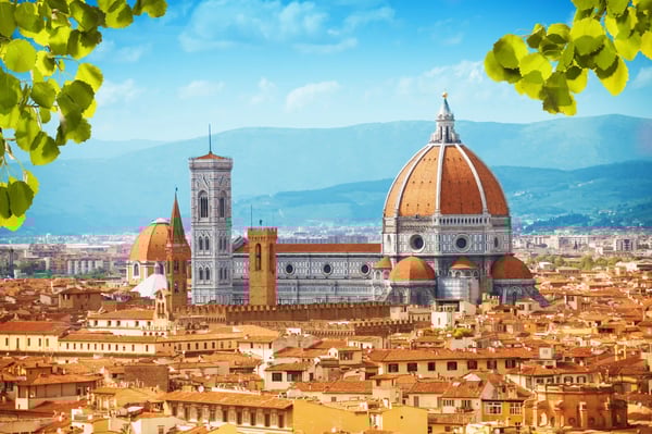 Panorama von Florenz mit der Kathedrale Santa Maria del Fiore und ihrer grossen roten Kuppel, dahinter Hügel und Berge unter blauem Himmel.