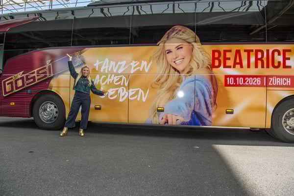 Beatrice Egli steht vor einem grossflächig gestalteten Reisebus mit farbigem Motiv und Schriftzug