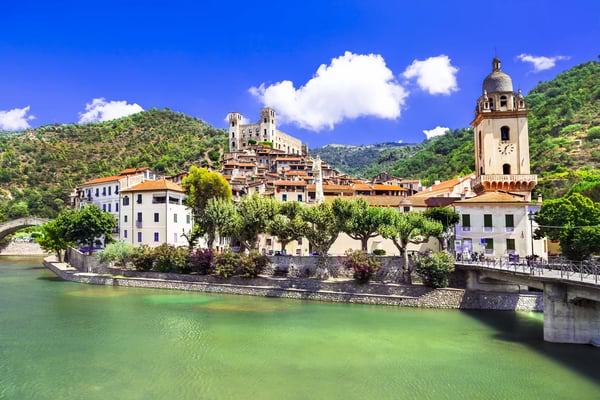 Malerisches Dorf Dolceacqua mit Steinbrücke, Kirche und historischen Häusern am Fluss, umgeben von grünen Hügeln unter blauem Himmel