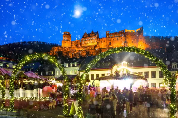 Weihnachtsmarkt in Heidelberg mit beleuchtetem Schloss im Hintergrund und fallendem Schnee