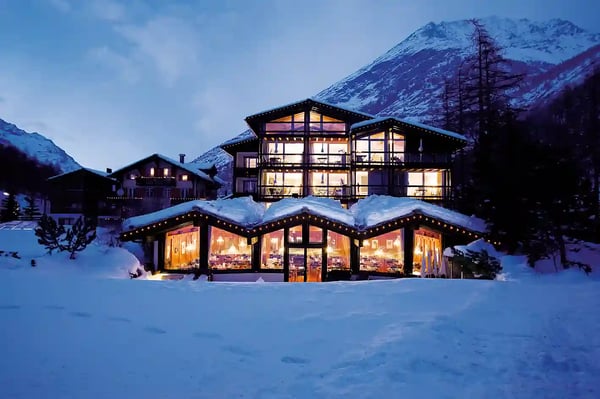 Modernes Hotel in verschneiter Berglandschaft mit beleuchteten Innenräumen bei Dämmerung