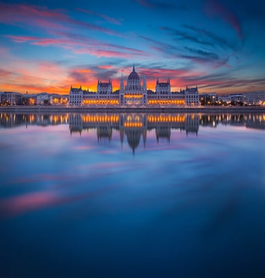 Ungarisches Parlamentsgebäude in Budapest bei Sonnenuntergang mit Spiegelung im ruhigen Wasser der Donau