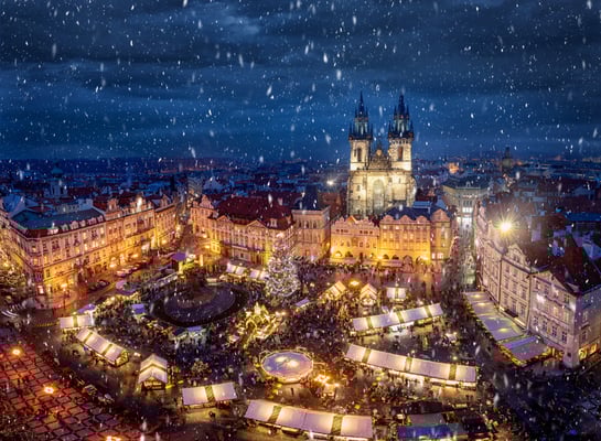 Belebter Weihnachtsmarkt in Prag mit geschmücktem Baum und fallendem Schnee
