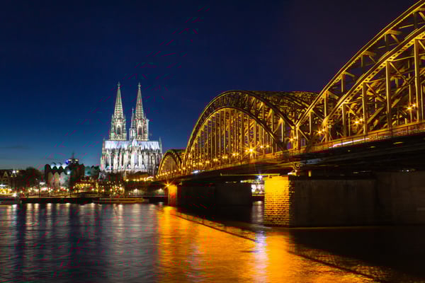 Kölner Dom und Hohenzollernbrücke bei Nacht, beleuchtet und spiegelnd im Rhein.